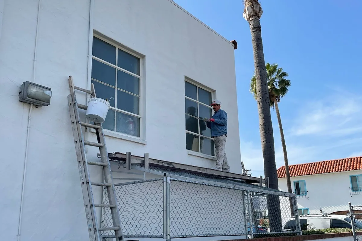 Tony's Painting crew member on a ladder painting a white stucco commercial building under palm trees, San Diego County