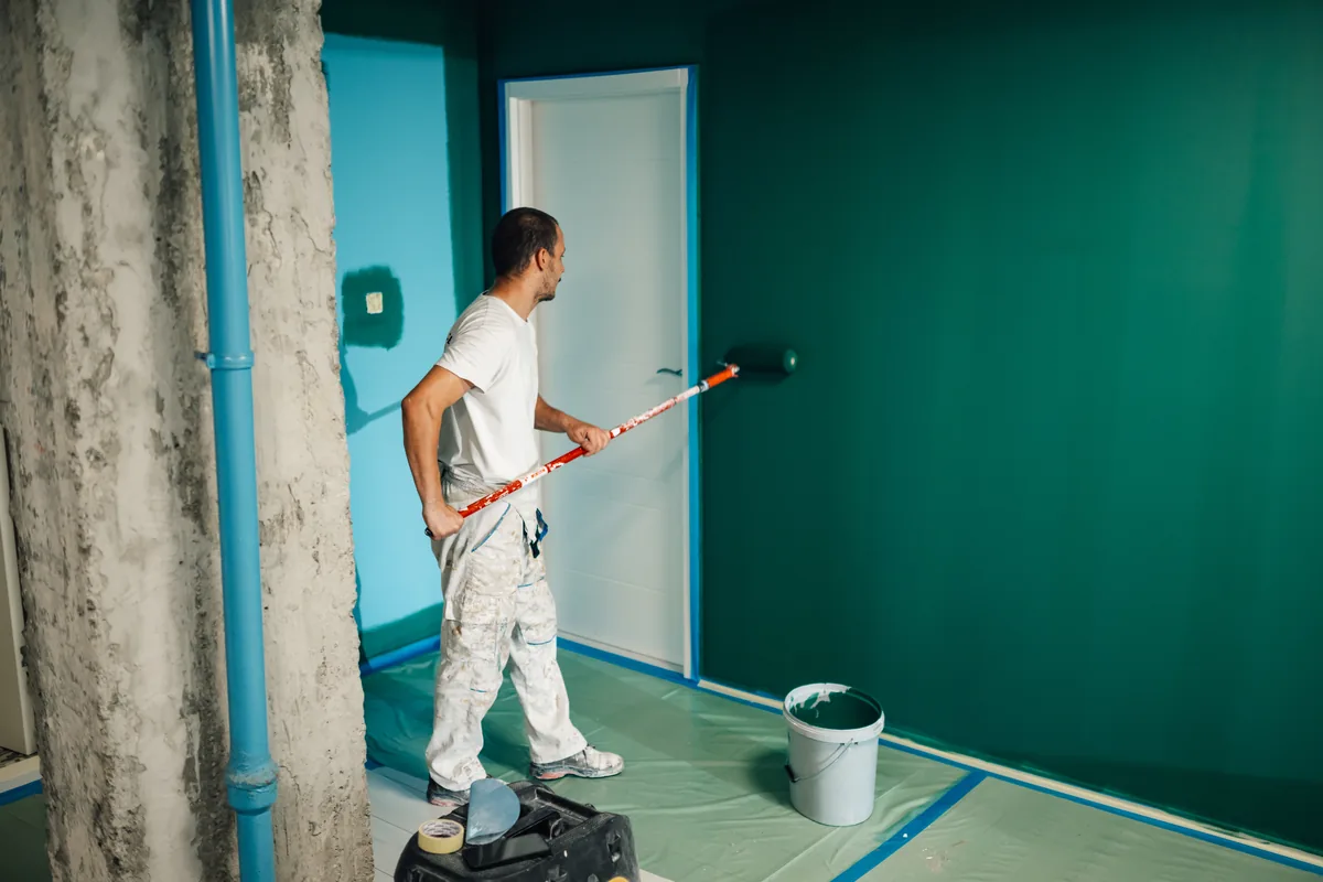 Painter rolling a deep teal wall in a multi-unit interior with the floor masked
