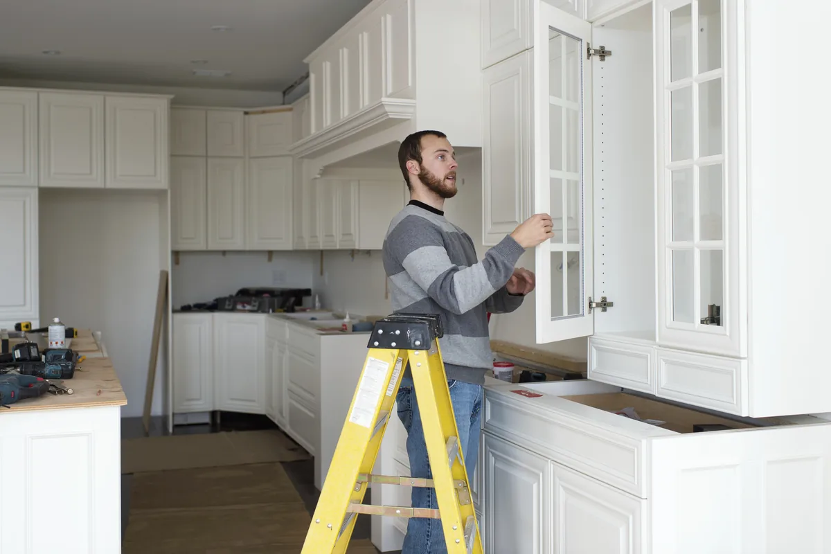 Glass-front upper cabinet door being fitted in a white kitchen