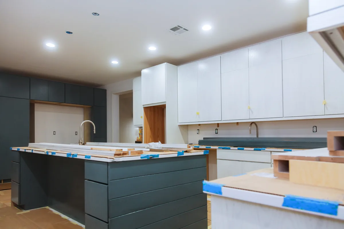 White kitchen cabinets and a blue island masked with painter's tape before finishing