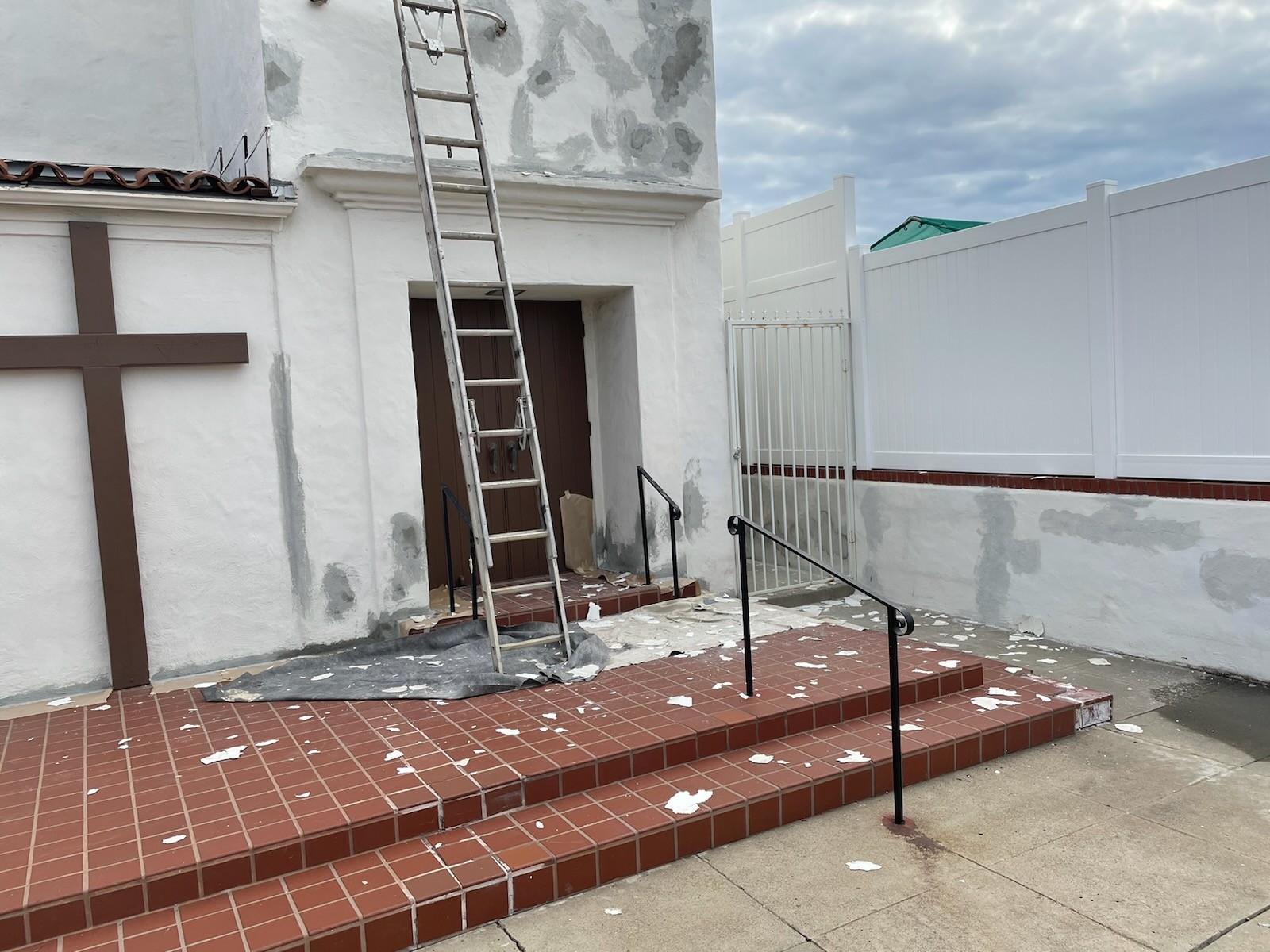 Restoration painting in progress at Good Shepherd Lutheran Church entry — ladder, prep, brown door trim mid-restoration.